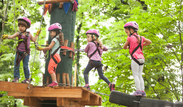 4 kids on ropes course strapped in wearing pink helmets