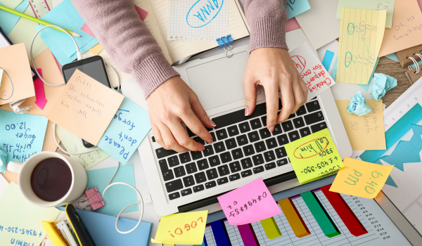 Woman working on laptop surrounded by sticky notes and coffee, representing mental load, overwhelm, and an irritable mom managing many tasks