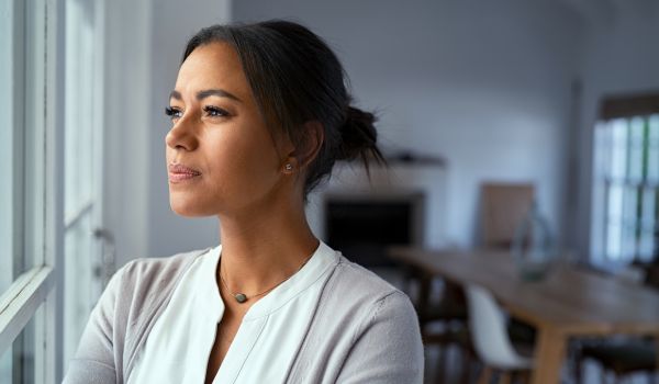 Woman looking out a window appearing tired and overwhelmed, representing mom burnout and emotional exhaustion