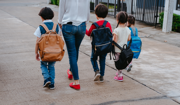 Mother walking with three children, appearing thoughtful and overwhelmed while managing daily responsibilities of motherhood
