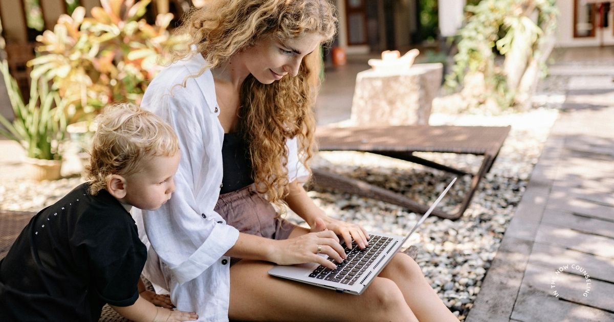 mom on computer with young child outside managing mental load this summer
