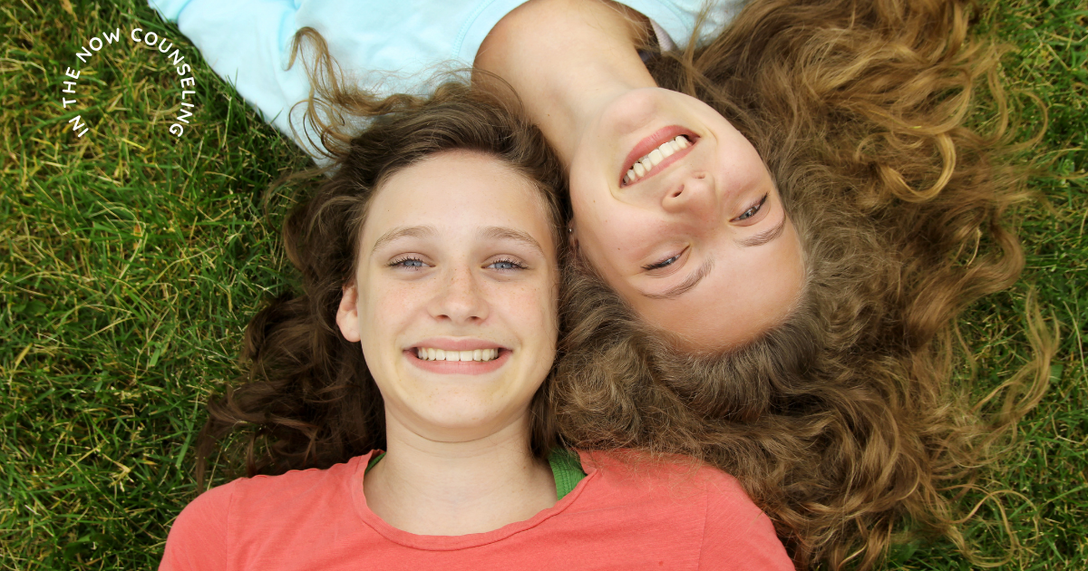 2 teens laying on grass with their heads touching smiling, representing relaxed behavior and not anxiety in kids