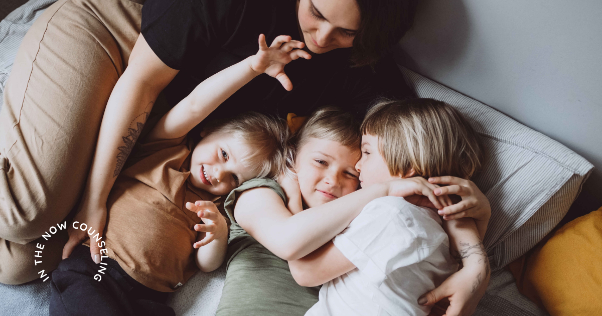 mom laying in a bed with 3 kids during the day showing why parenting can feel harder in summer